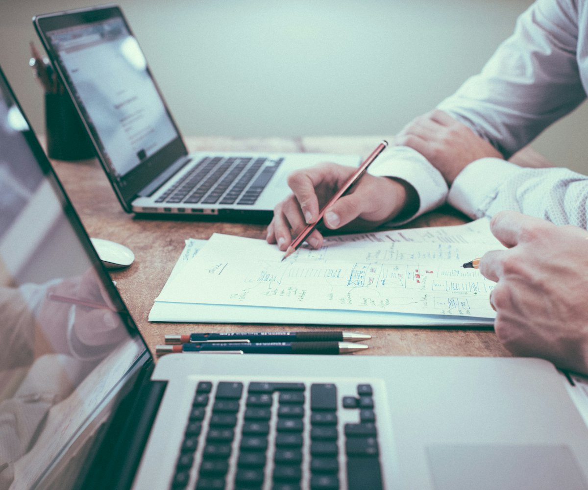 Hands reviewing printed documents beside laptops during procurement planning